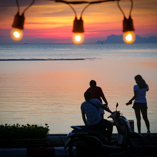 Friends silhouetted against string lights at sunset
