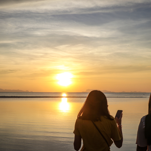 Woman photographing the sunset over water